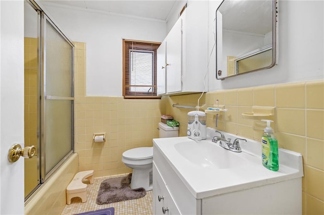 bathroom with toilet, shower / bath combination with glass door, tile patterned floors, vanity, and tile walls