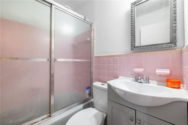 full bath with toilet, a wainscoted wall, vanity, tile walls, and combined bath / shower with glass door