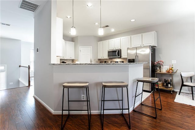 kitchen with dark wood finished floors, visible vents, appliances with stainless steel finishes, a peninsula, and a kitchen breakfast bar