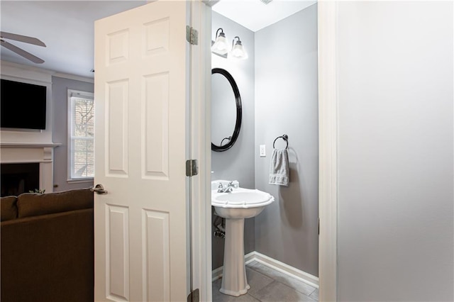 bathroom featuring baseboards, a ceiling fan, tile patterned flooring, a fireplace, and a sink