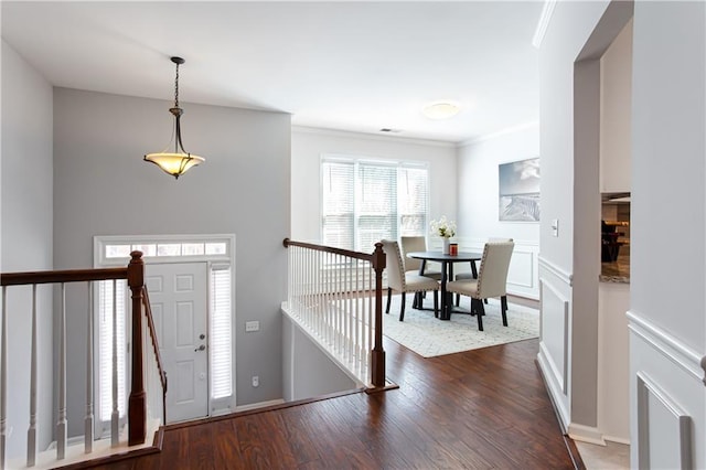 foyer with a decorative wall, wainscoting, wood finished floors, and crown molding