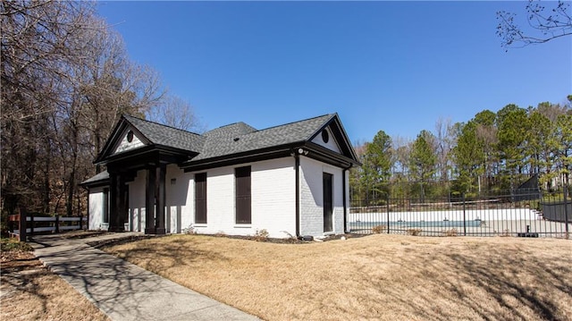 view of side of property featuring a fenced in pool, brick siding, a shingled roof, a lawn, and fence