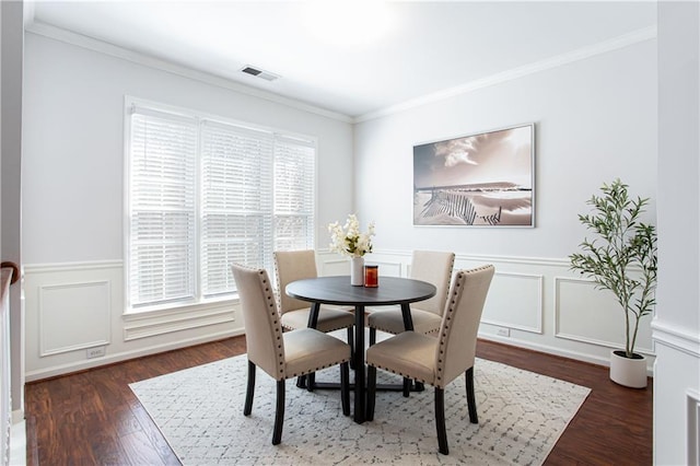 dining area with a decorative wall, a wainscoted wall, dark wood-style flooring, visible vents, and ornamental molding