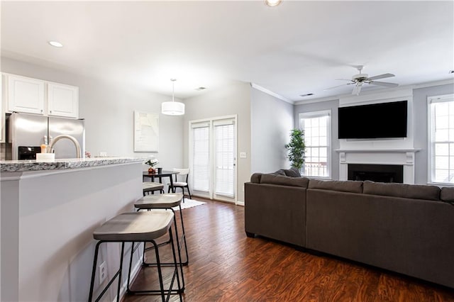 living room with a ceiling fan, dark wood-type flooring, crown molding, a fireplace, and recessed lighting