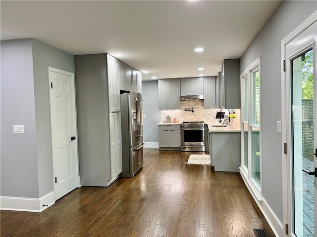 kitchen with appliances with stainless steel finishes, gray cabinets, backsplash, light countertops, and dark wood-style flooring