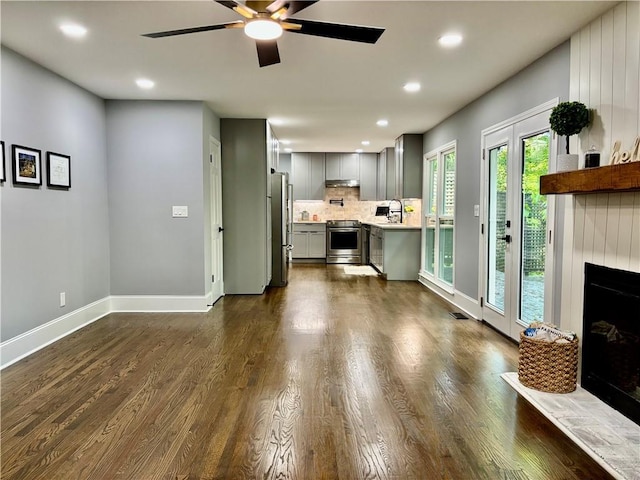 living area featuring ceiling fan, a fireplace with raised hearth, baseboards, dark wood-type flooring, and recessed lighting