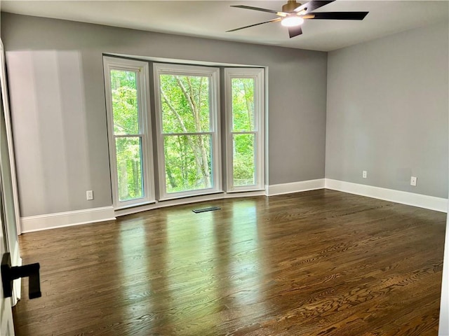 unfurnished room with plenty of natural light, a ceiling fan, baseboards, and dark wood finished floors