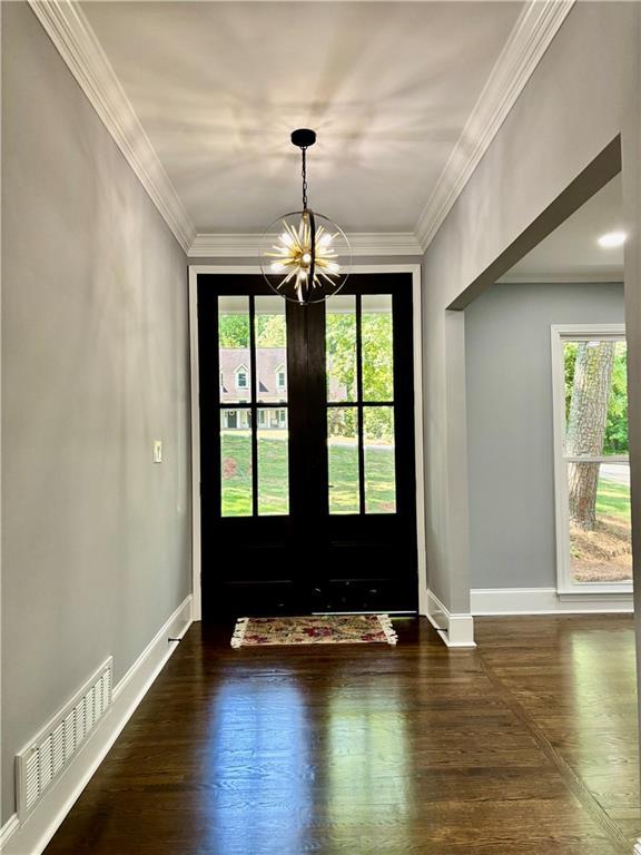 doorway to outside featuring a chandelier, healthy amount of natural light, baseboards, crown molding, and wood finished floors