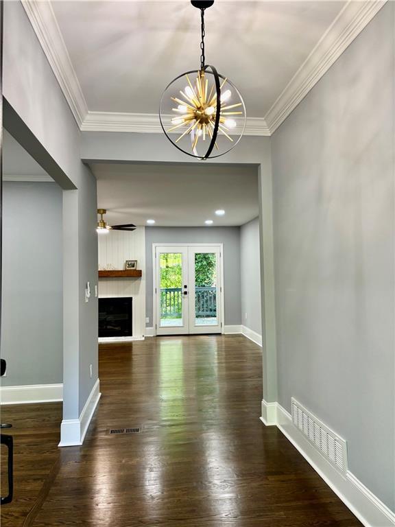 unfurnished living room featuring a chandelier, wood-type flooring, crown molding, a fireplace, and baseboards