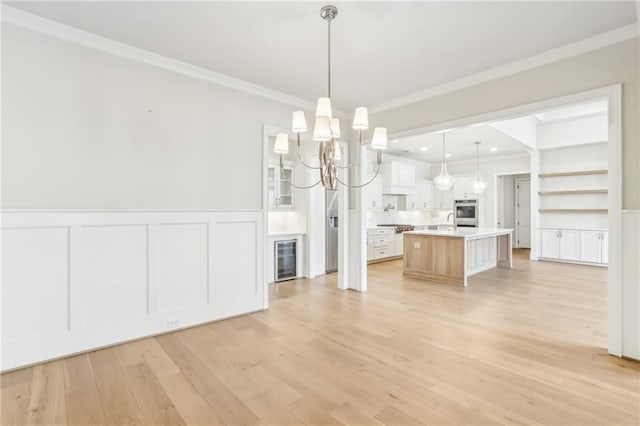 unfurnished dining area featuring ornamental molding, beverage cooler, light wood finished floors, and a wainscoted wall