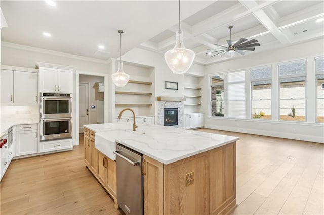 kitchen with light wood finished floors, appliances with stainless steel finishes, open floor plan, a sink, and coffered ceiling