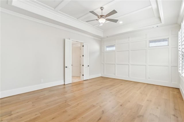 empty room with a raised ceiling, ceiling fan, ornamental molding, light wood-style floors, and a decorative wall