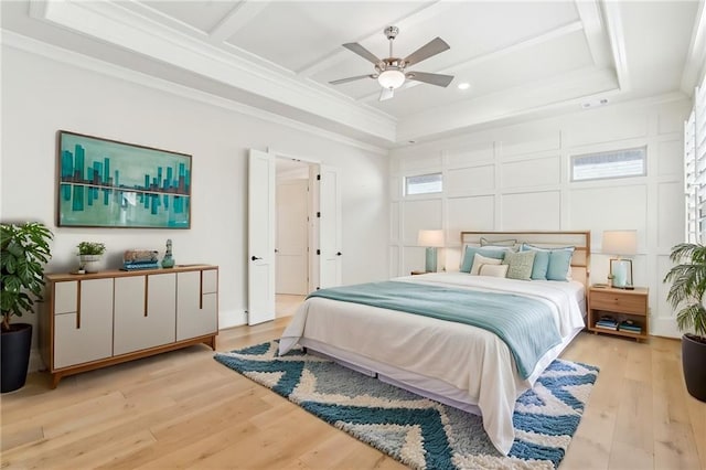 bedroom with crown molding, light wood finished floors, a raised ceiling, a decorative wall, and ceiling fan