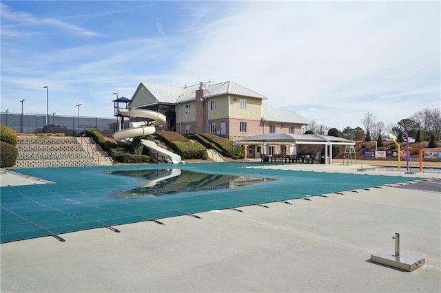 community pool with fence, a water slide, and a patio