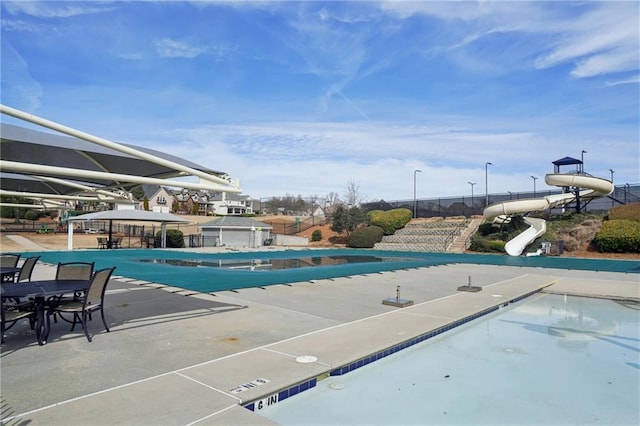 pool featuring a water slide, fence, and a patio