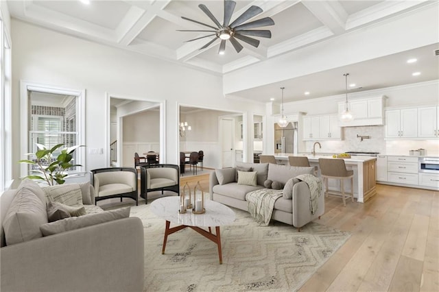 living area featuring beam ceiling, light wood finished floors, ornamental molding, a ceiling fan, and coffered ceiling