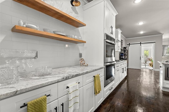 kitchen with a barn door, stainless steel double oven, dark wood-style floors, open shelves, and ornamental molding