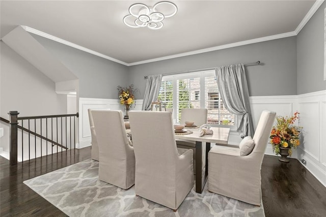 dining room featuring wood finished floors, a decorative wall, ornamental molding, and wainscoting