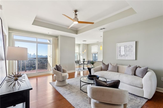 living room with ceiling fan, wood-type flooring, and a tray ceiling