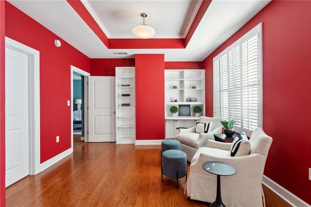 sitting room with hardwood / wood-style flooring, crown molding, and a raised ceiling