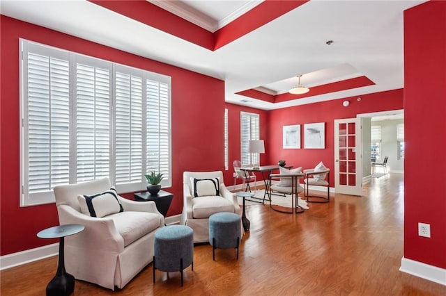 living area featuring wood-type flooring, crown molding, and a tray ceiling