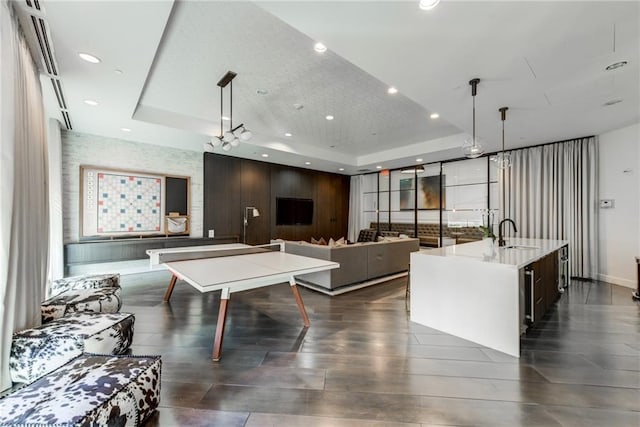 recreation room featuring a raised ceiling, sink, and dark wood-type flooring