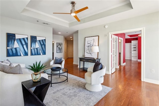 living room with ceiling fan, wood-type flooring, and a raised ceiling