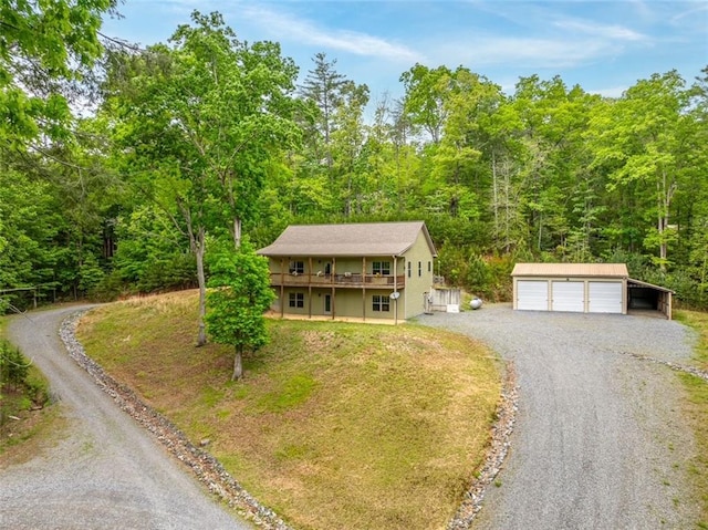 view of front of property featuring a detached garage, a deck, an outdoor structure, driveway, and a wooded view