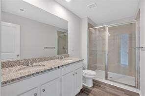 bathroom featuring toilet, a sink, wood finished floors, a shower stall, and double vanity