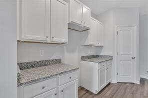 kitchen featuring wood finished floors, white cabinetry, and light stone countertops