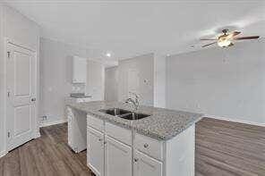 kitchen featuring a kitchen island with sink, dark wood-type flooring, a sink, white cabinets, and dishwasher