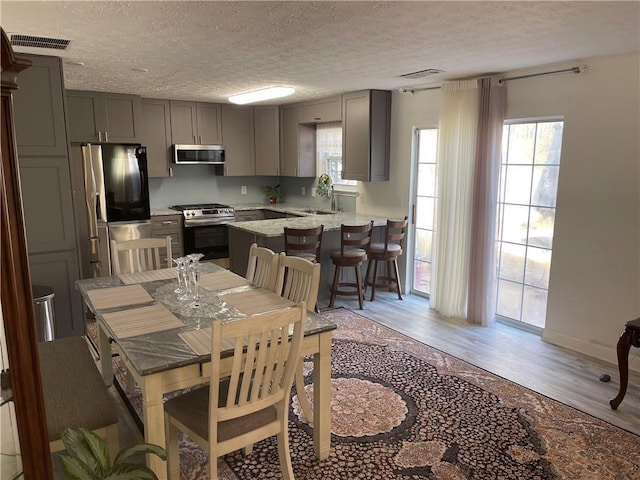 kitchen featuring light wood-type flooring, stainless steel range, a textured ceiling, exhaust hood, and gray cabinets