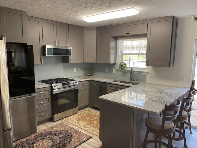 kitchen featuring gray cabinetry, kitchen peninsula, sink, and appliances with stainless steel finishes