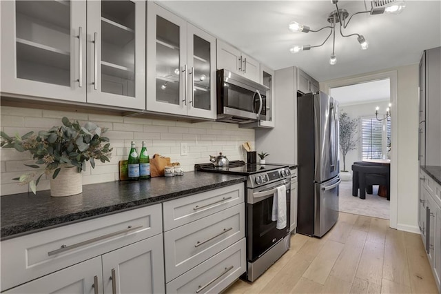 kitchen featuring a chandelier, light hardwood / wood-style flooring, dark stone counters, stainless steel appliances, and decorative backsplash