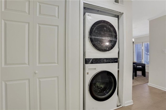 clothes washing area with stacked washer / drying machine, ornamental molding, and light wood-type flooring