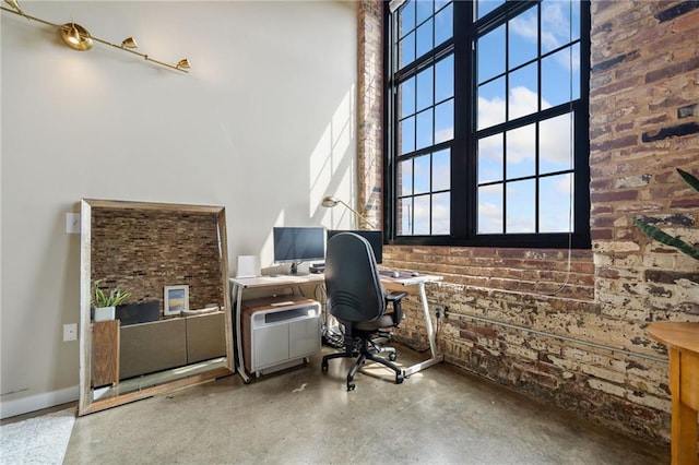 office area with a high ceiling, concrete flooring, and brick wall