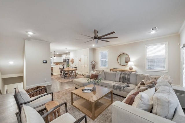 living room with crown molding, ceiling fan with notable chandelier, and light hardwood / wood-style floors