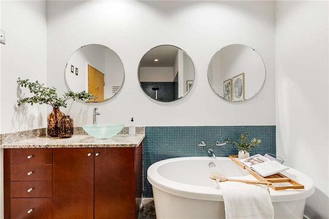 full bathroom featuring tile walls, a soaking tub, vanity, and a wainscoted wall