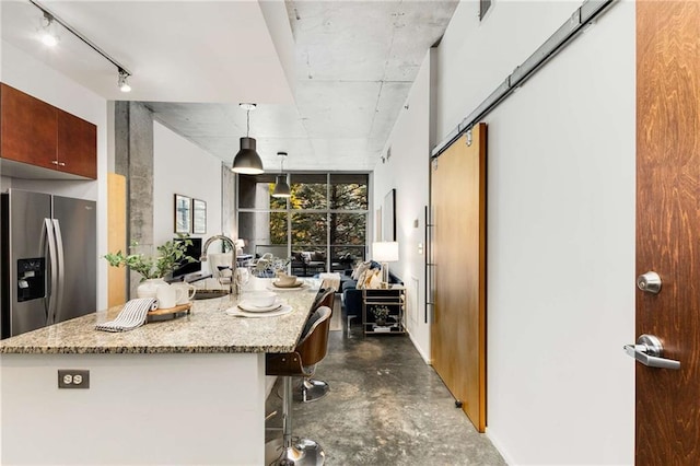 kitchen with light stone counters, a sink, stainless steel fridge with ice dispenser, a breakfast bar area, and concrete floors