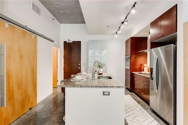 kitchen featuring a barn door, a sink, an island with sink, stainless steel appliances, and visible vents
