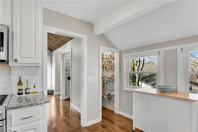 kitchen featuring lofted ceiling with beams, tasteful backsplash, wood finished floors, white cabinets, and baseboards