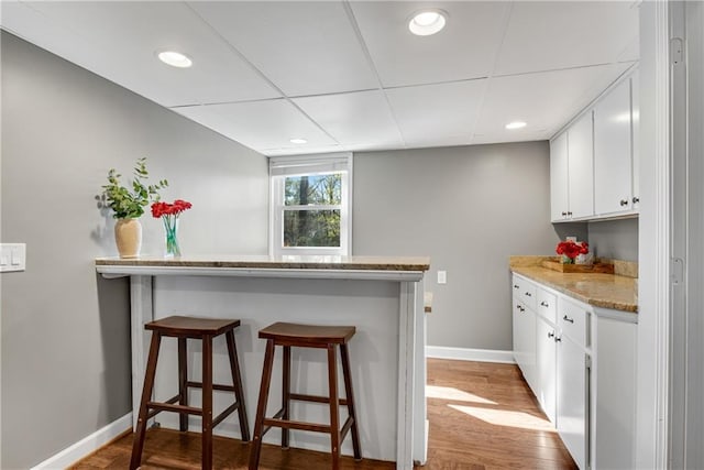 kitchen featuring baseboards, a breakfast bar, a peninsula, white cabinets, and light wood-type flooring