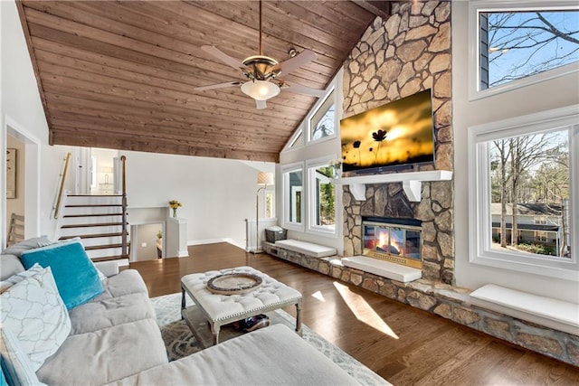 living room with wood finished floors, high vaulted ceiling, a stone fireplace, stairs, and wooden ceiling