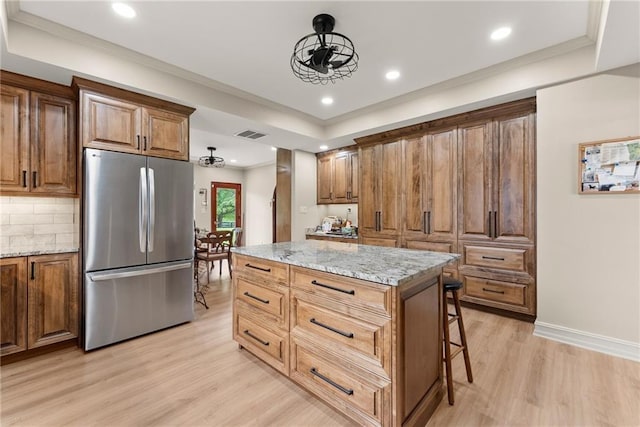 kitchen with crown molding, light wood finished floors, freestanding refrigerator, and light stone countertops