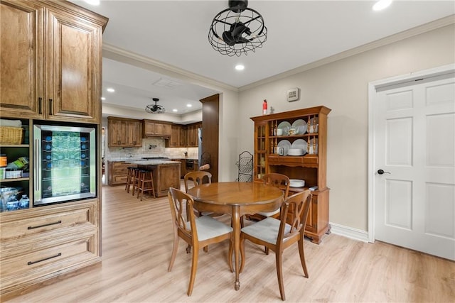 dining space with beverage cooler, light wood-style floors, baseboards, and crown molding