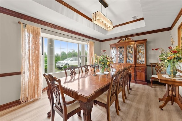 dining space with a tray ceiling, crown molding, visible vents, light wood-style flooring, and baseboards