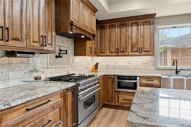 kitchen with stainless steel appliances, brown cabinetry, a sink, and light stone countertops