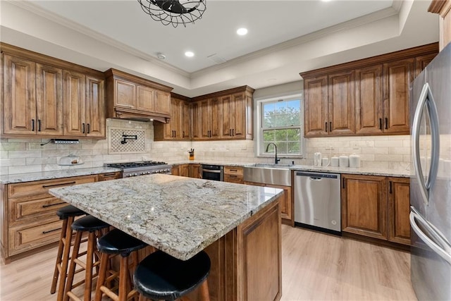 kitchen with stainless steel appliances, light wood-type flooring, light stone countertops, a tray ceiling, and brown cabinetry