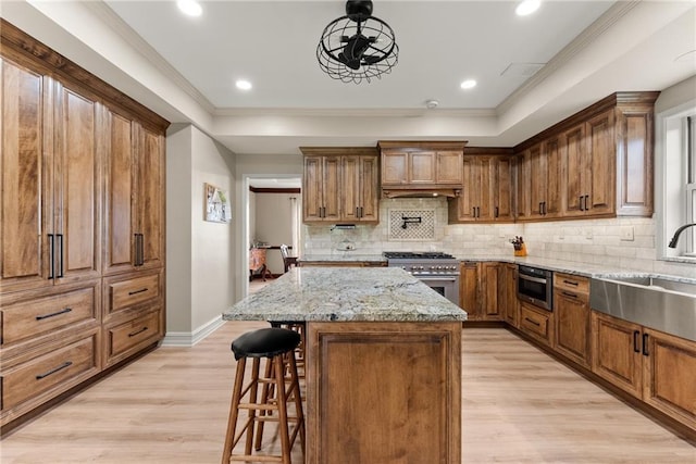 kitchen featuring a sink, a kitchen breakfast bar, light wood-type flooring, light stone countertops, and stainless steel range