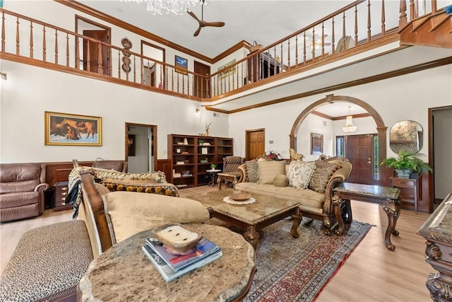 living area with arched walkways, crown molding, a towering ceiling, wood finished floors, and a chandelier